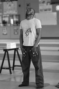 Professeur de yoga debout sur un tapis, yeux fermés, en posture de respiration consciente dans une salle intérieure.